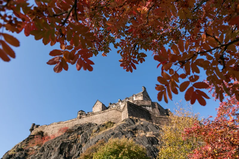 Edinburgh castle perched on volcanic rock viewed from below through autumn foliage