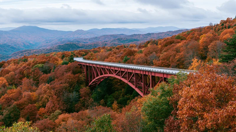 Red steel viaduct spanning a forested valley in autumn with mountains in the background
