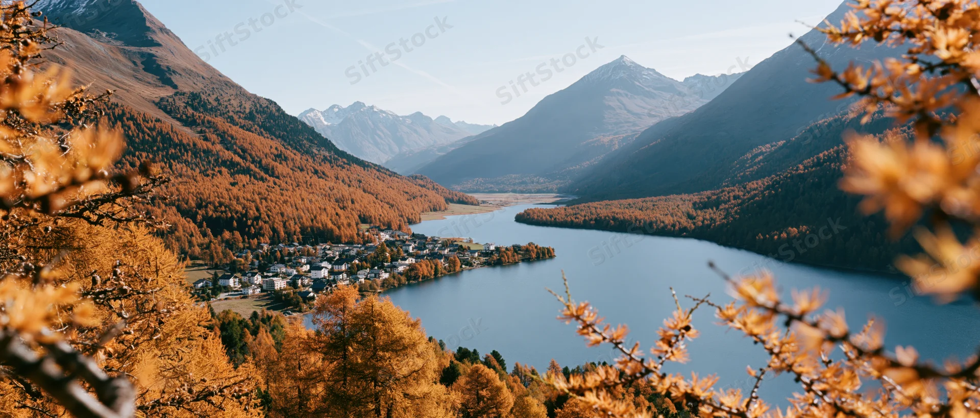 Panoramic view of alpine village beside lake surrounded by autumn-colored mountains