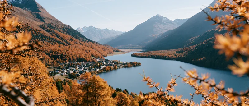 Panoramic view of alpine village beside lake surrounded by autumn-colored mountains