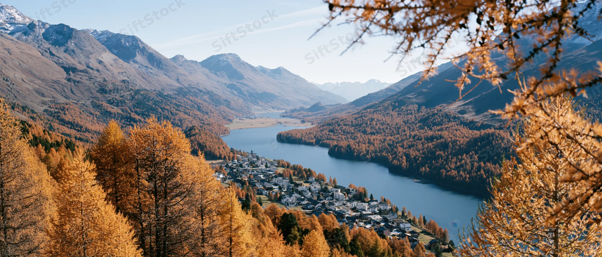 Elevated panoramic view of alpine village beside mountain lake surrounded by autumn trees