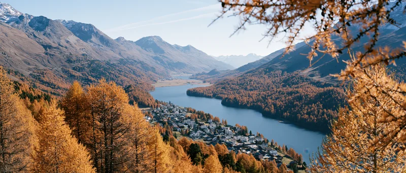 Elevated panoramic view of alpine village beside mountain lake surrounded by autumn trees
