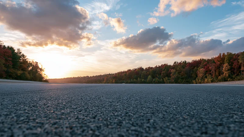 Empty asphalt race track stretching to a treeline of autumn trees at sunset