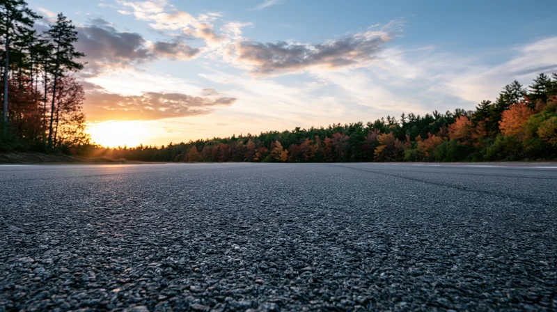 Empty asphalt race track stretching toward a treeline at sunset