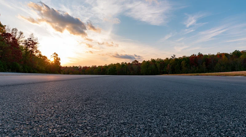 Empty asphalt track stretching toward a treeline at sunset