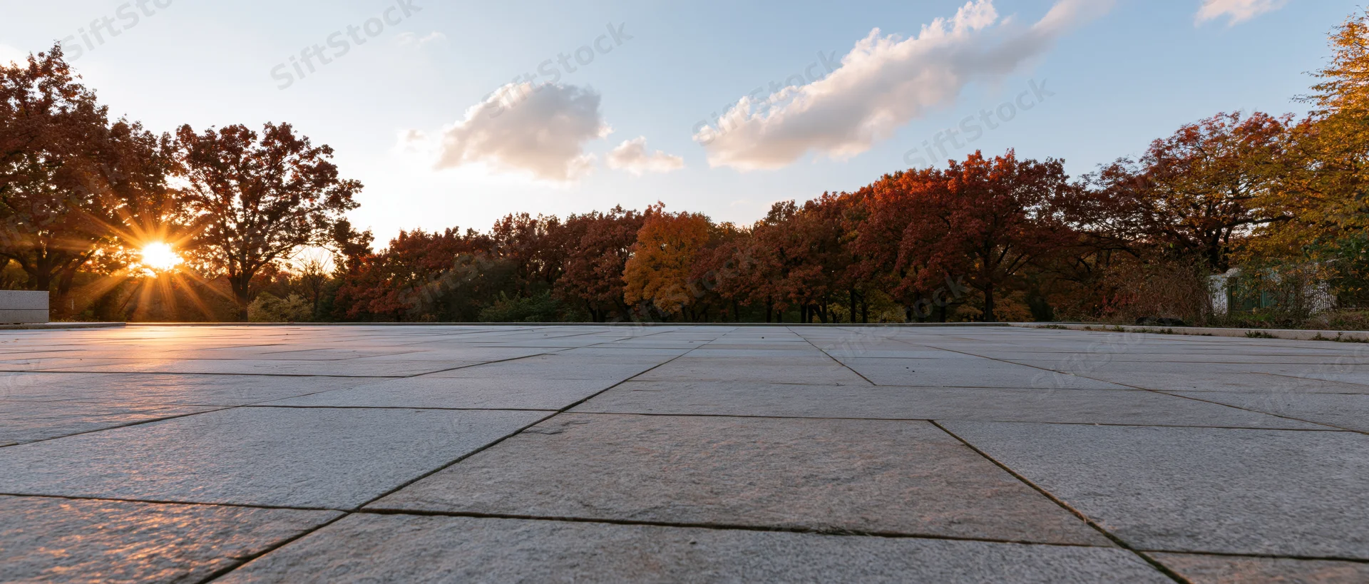 Empty granite-tiled plaza stretching to horizon at sunset with autumn trees in background
