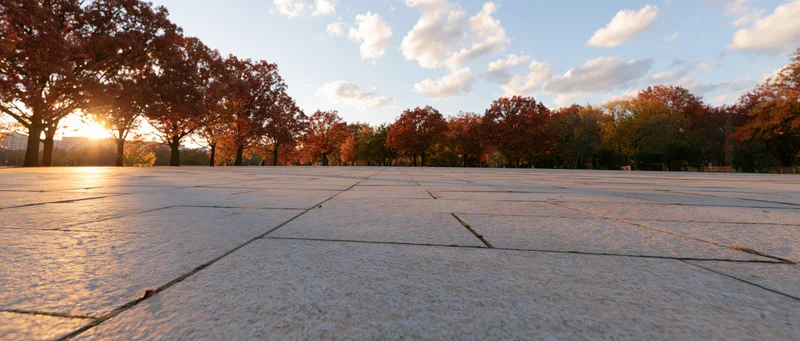 Granite-tiled plaza stretching toward autumn trees at sunset
