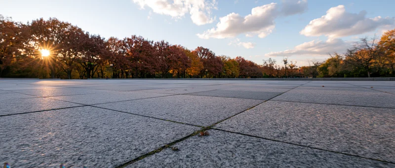Empty granite-tiled plaza stretching to horizon at sunset with autumn trees in background