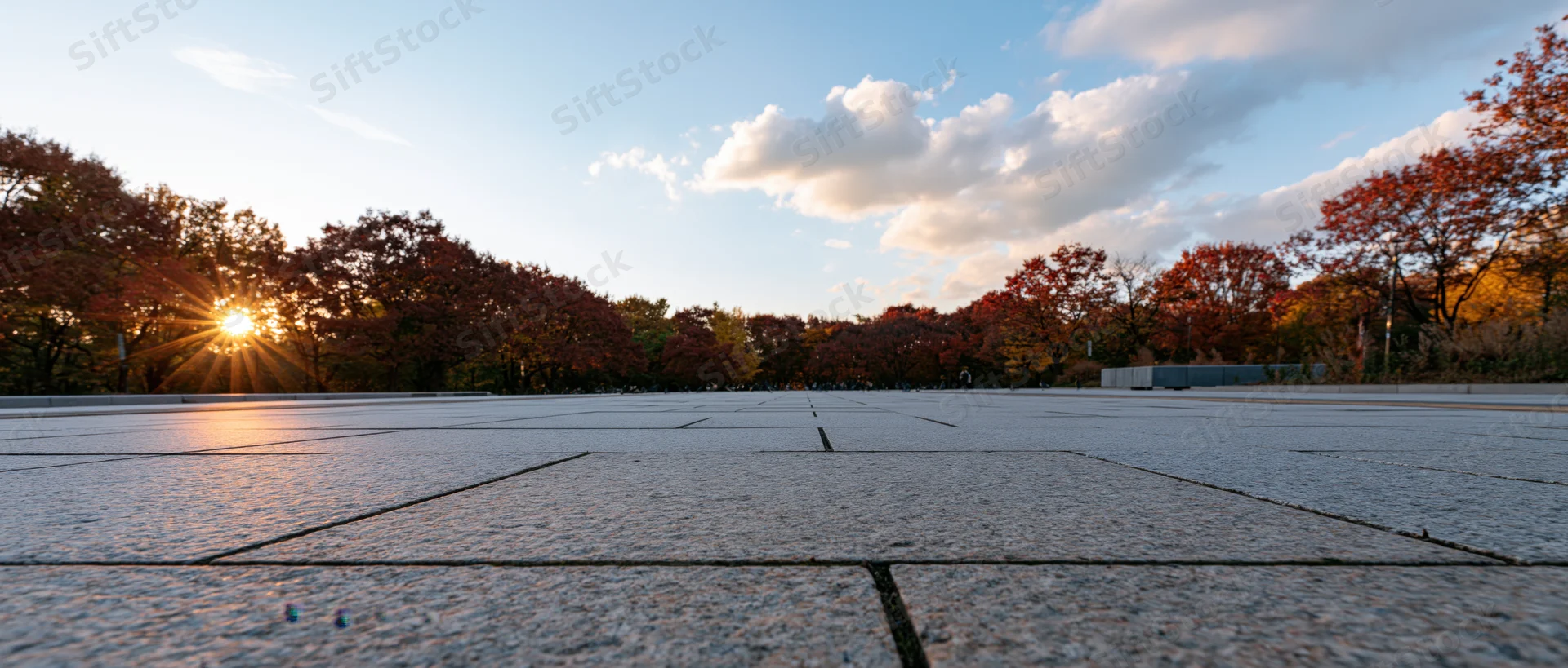 Granite-tiled plaza stretching to the horizon at sunset with autumn trees lining the edges