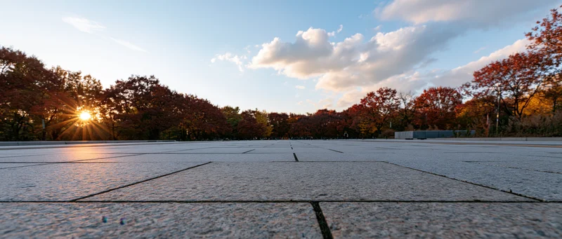 Granite-tiled plaza stretching to the horizon at sunset with autumn trees lining the edges