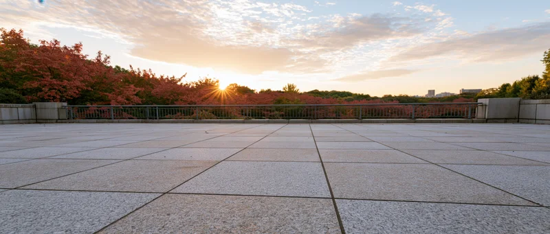 Empty granite-tiled plaza at sunset with metal railing and autumn trees in the distance