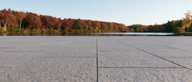 Grey granite tiles of a plaza extending to a still lake surrounded by autumn trees