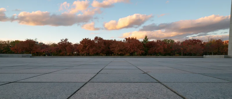 Wide stone-tiled plaza leading to autumn trees under soft sunset sky