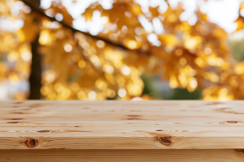 Light pine wooden table surface in front of blurred autumn foliage outdoors