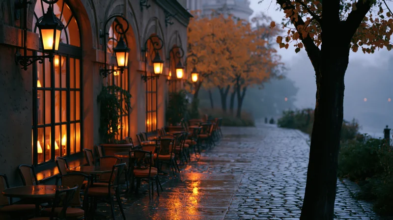 Empty outdoor cafe terrace with tables and chairs on a wet cobblestone street at dusk