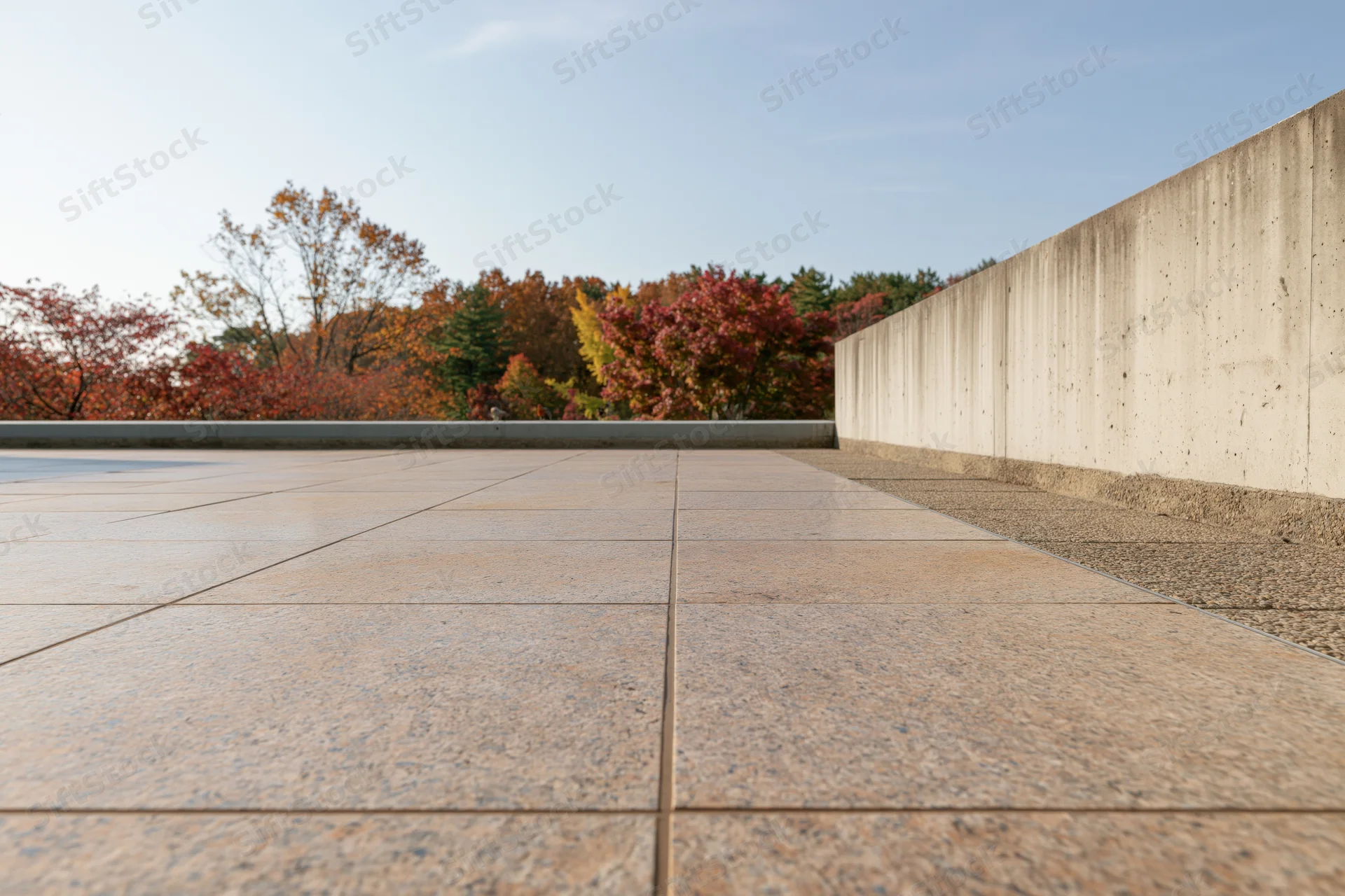 Polished granite plaza extending toward autumn trees under clear sky