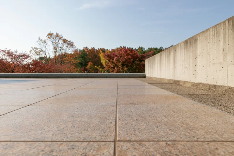 Polished granite plaza extending toward autumn trees under clear sky