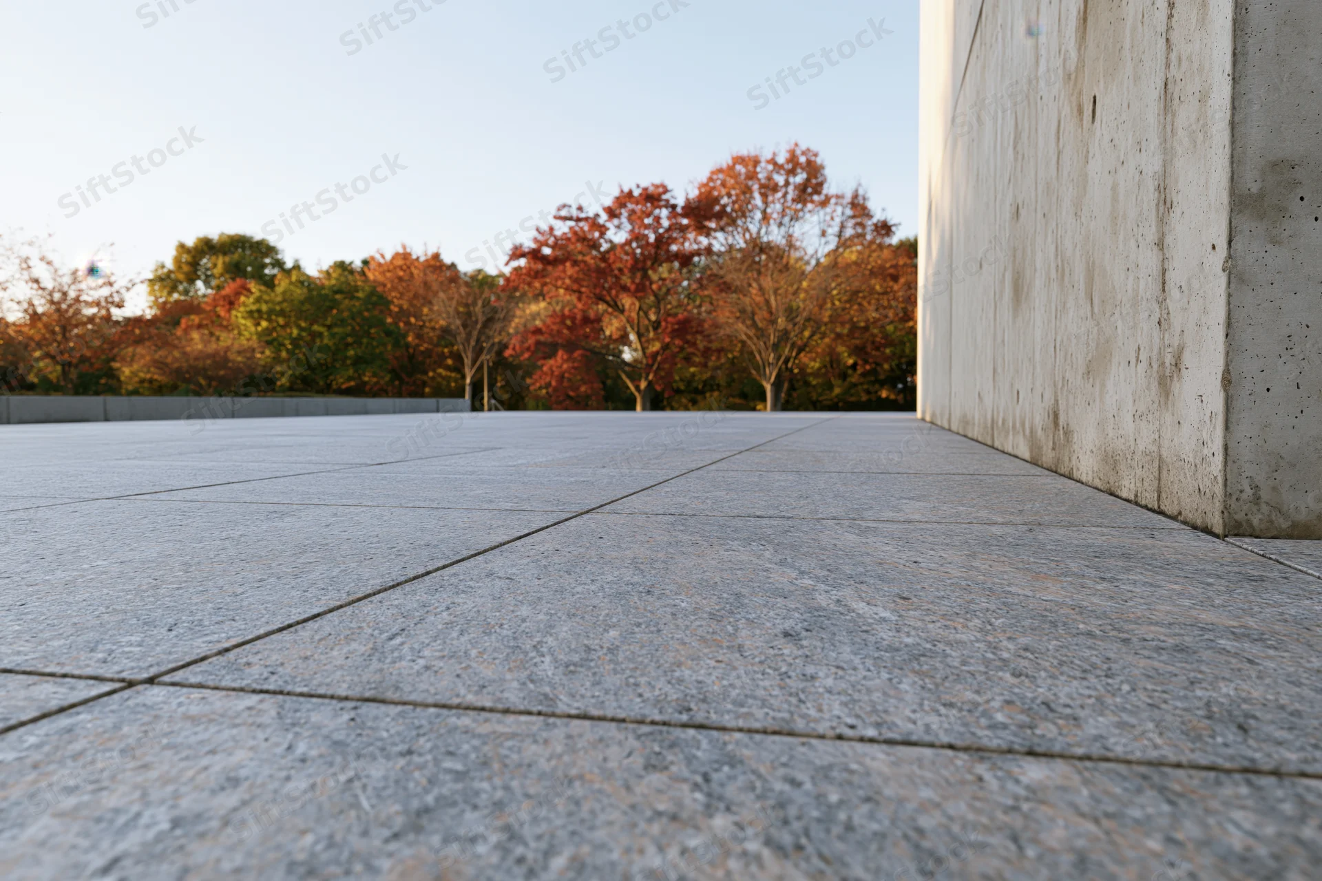Polished granite plaza stretching toward a treeline of autumn trees under clear sky