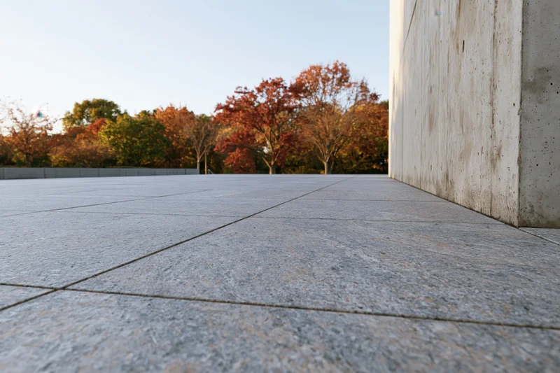 Polished granite plaza stretching toward a treeline of autumn trees under clear sky