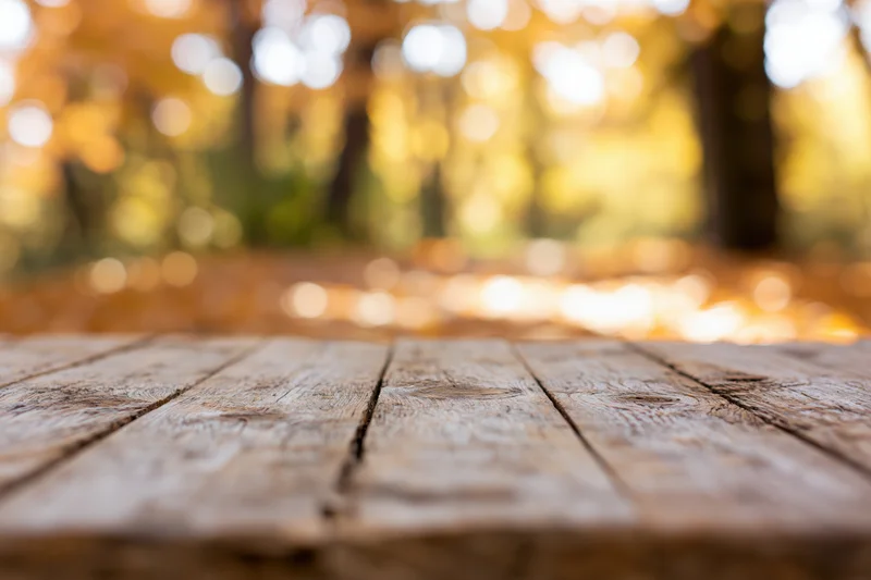 Rustic wooden table surface in a forest with autumn foliage and bokeh background