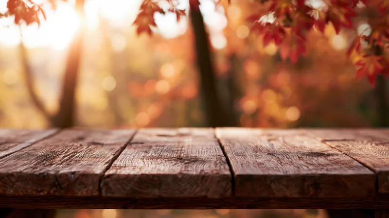 Rustic wooden table surface in autumn forest with red leaves and warm sunlight in background