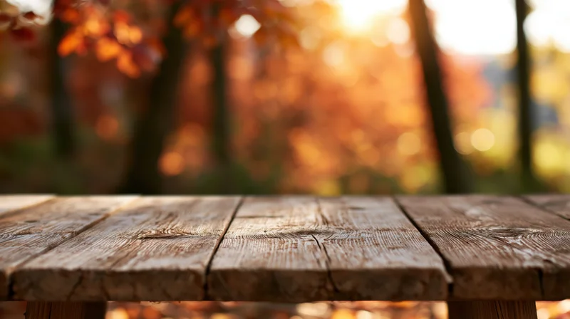 Rustic wooden table surface in a forest during autumn with warm sunlight and blurred foliage in the background