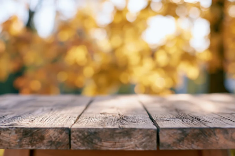 Rustic wooden table surface in outdoor setting with autumn foliage blurred in background