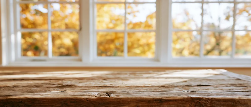 Rustic wooden tabletop in foreground with autumn foliage visible through white paned window