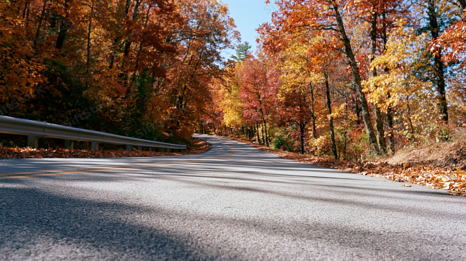 Winding asphalt road curving through autumn forest with colorful foliage and guardrail on side