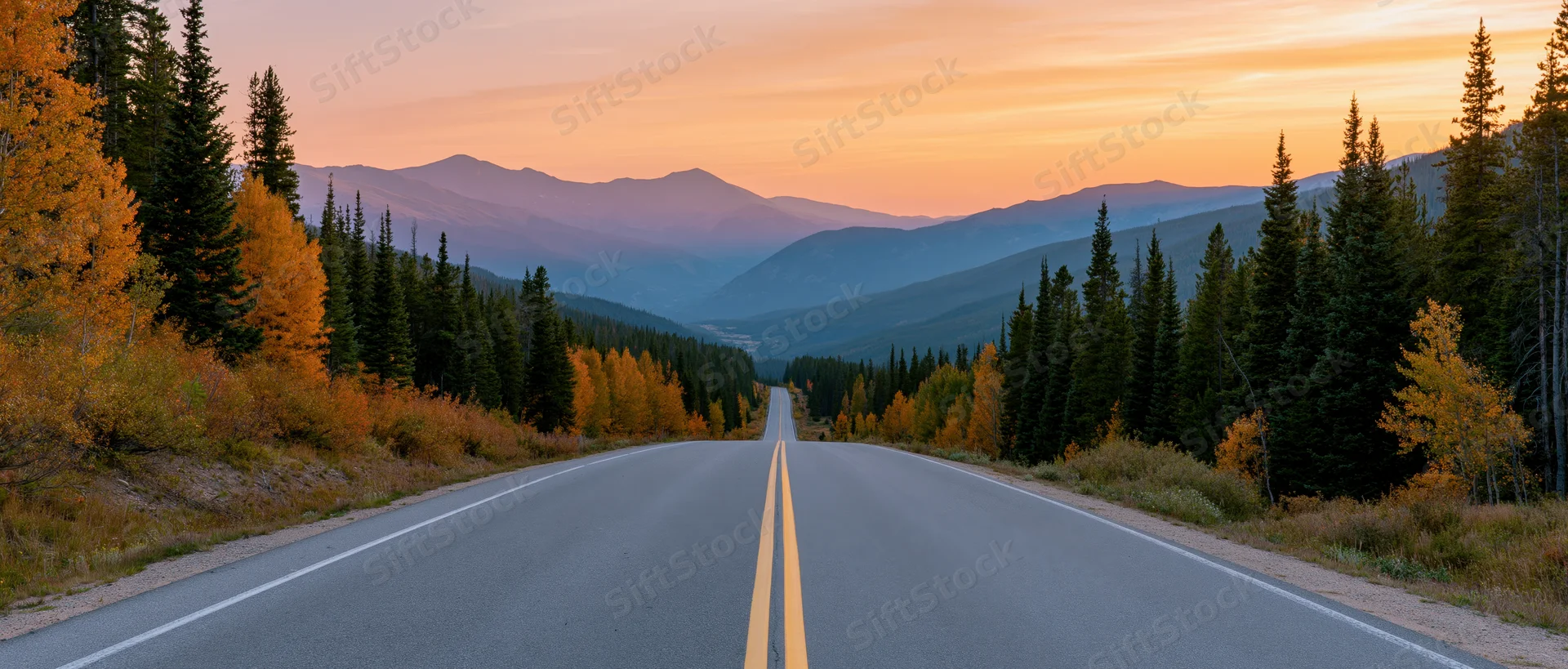 Two-lane highway stretching toward distant mountains at sunset through autumn forest