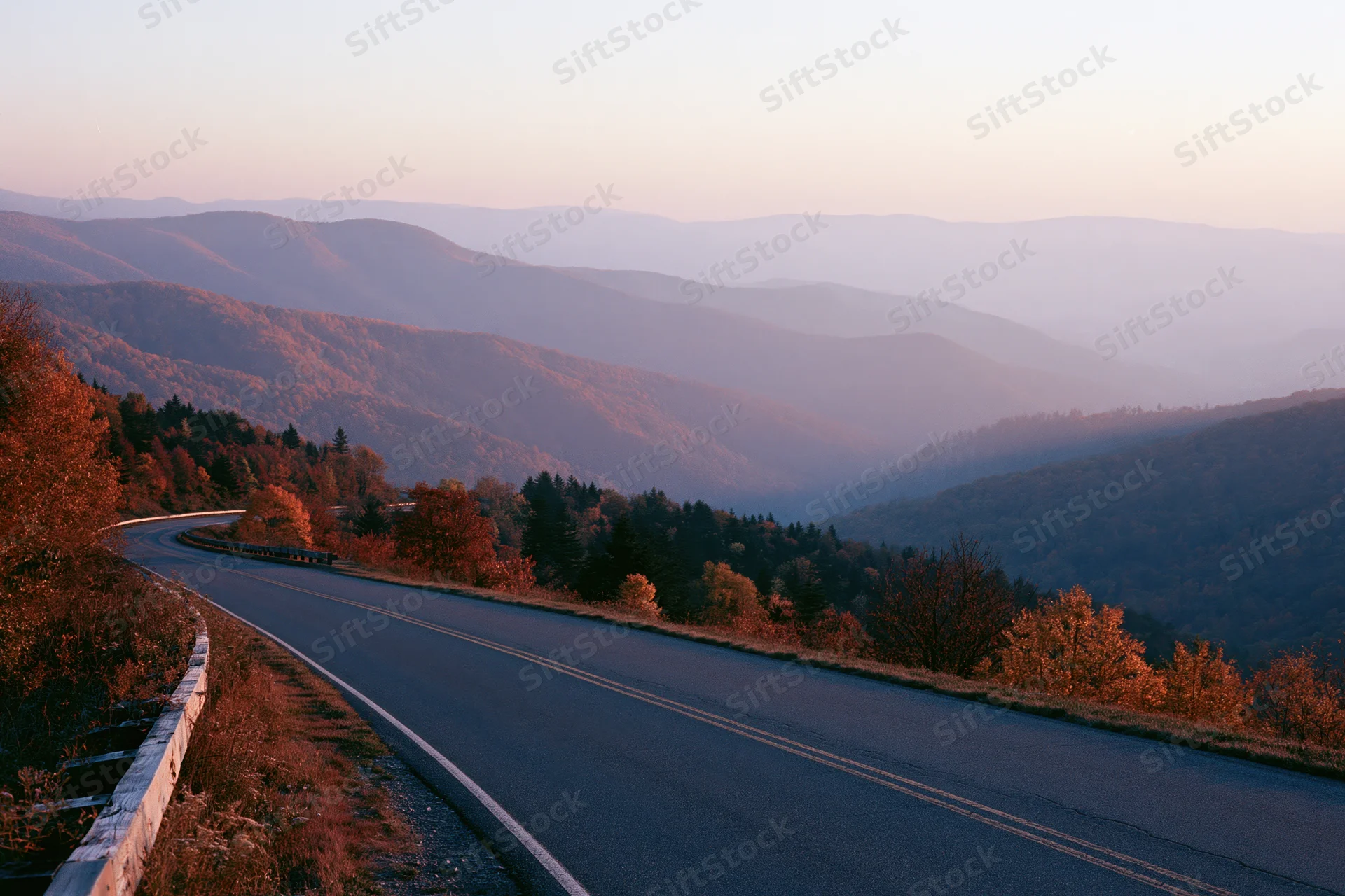 Winding two-lane road curves through forested mountains at sunset