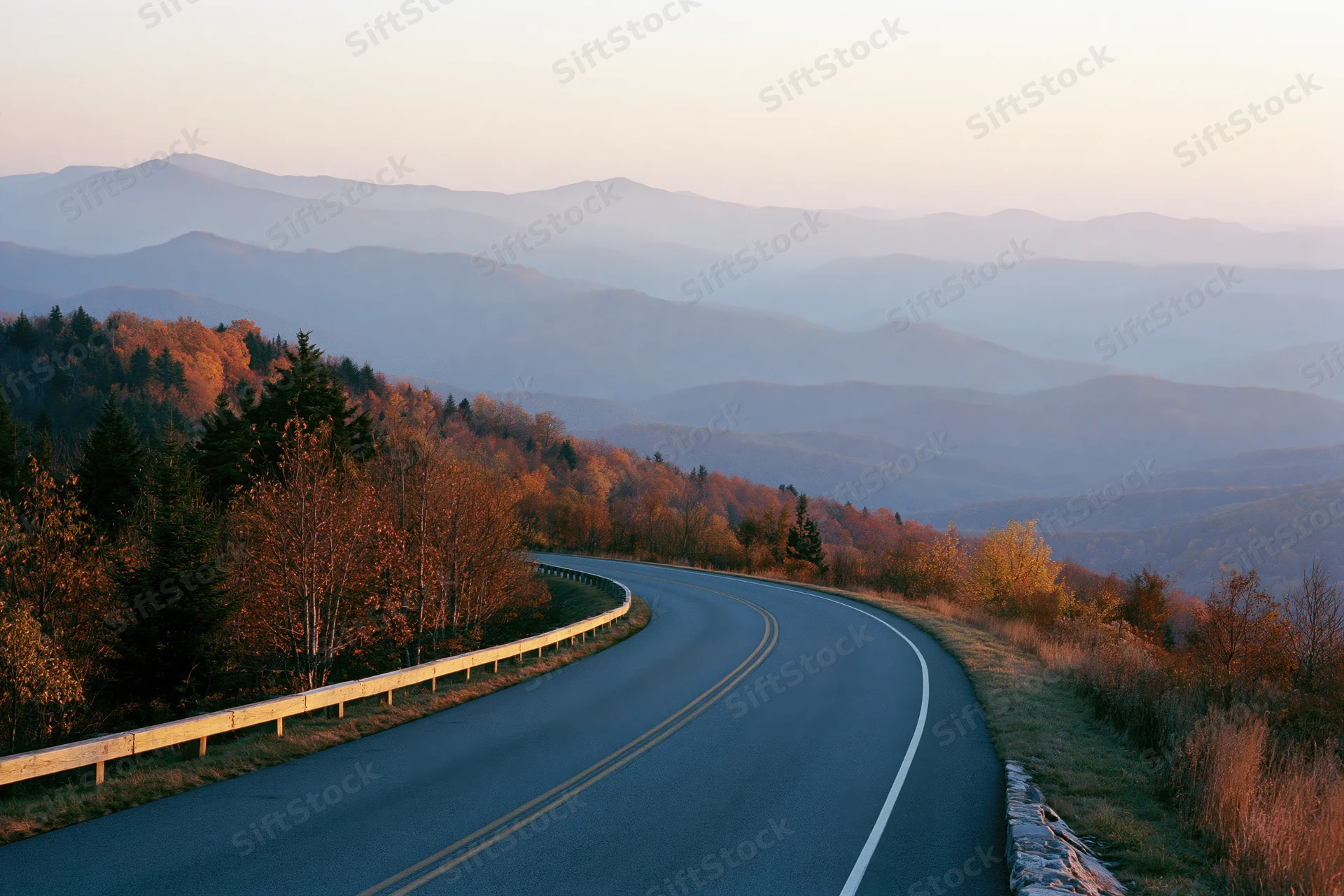 Winding two-lane road curves through autumn forested mountains at sunset