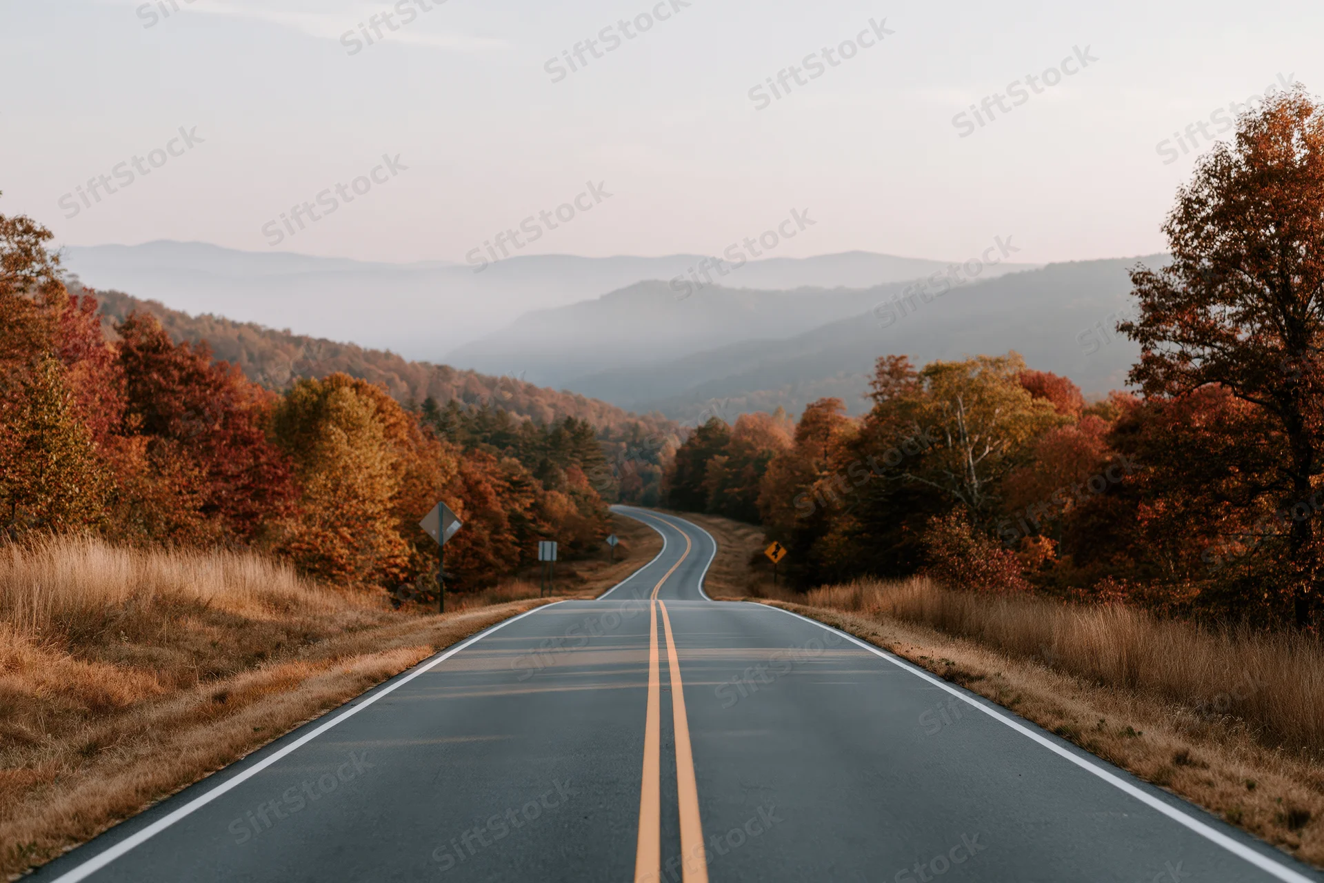 Winding two-lane highway through autumn forest toward misty mountains