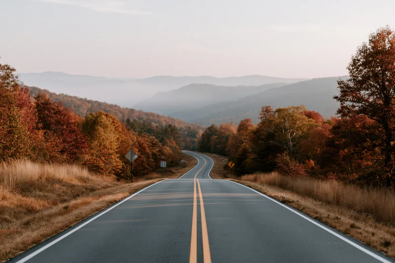 Winding two-lane highway through autumn forest toward misty mountains