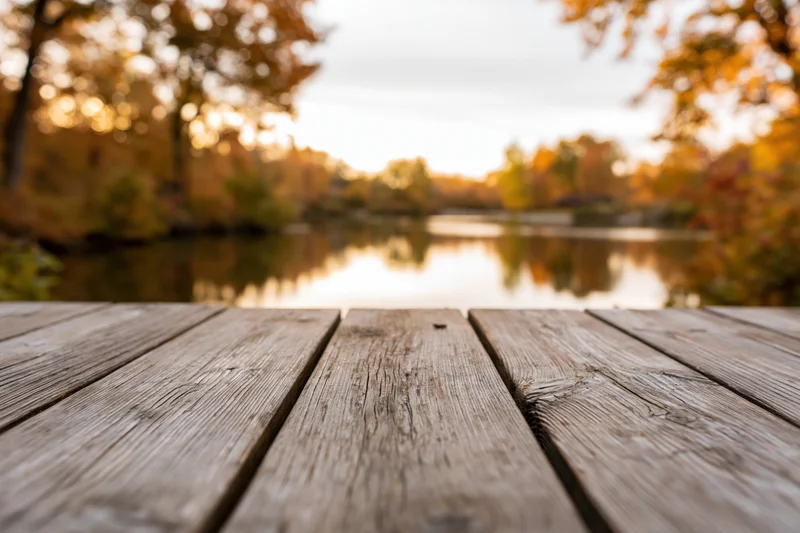 Weathered wooden table in foreground overlooking lake surrounded by autumn trees at sunset