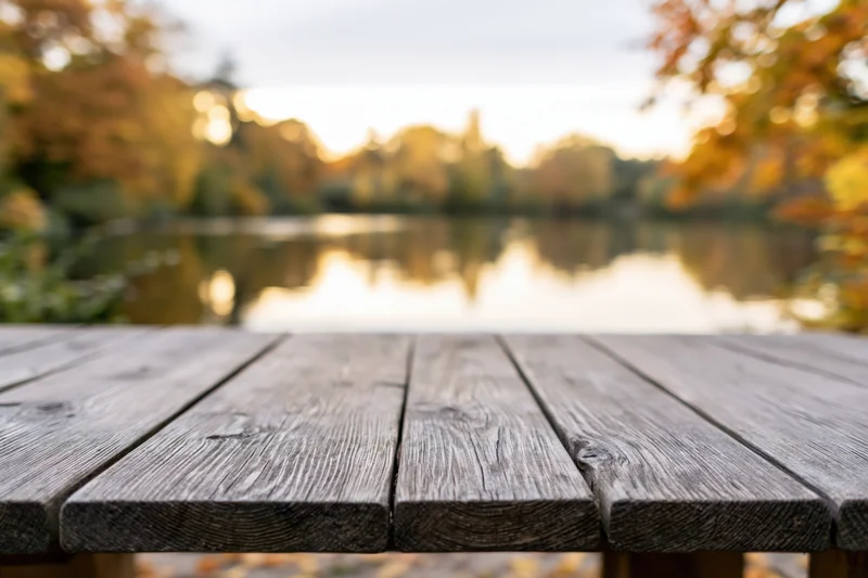 Weathered wooden table in foreground overlooking lake surrounded by autumn trees at sunset