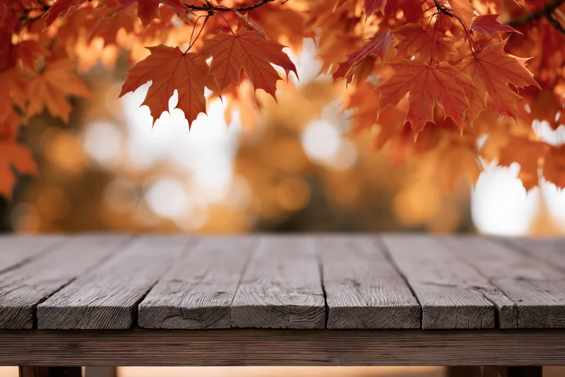Weathered wooden table surface in front of autumn maple leaves in a park setting