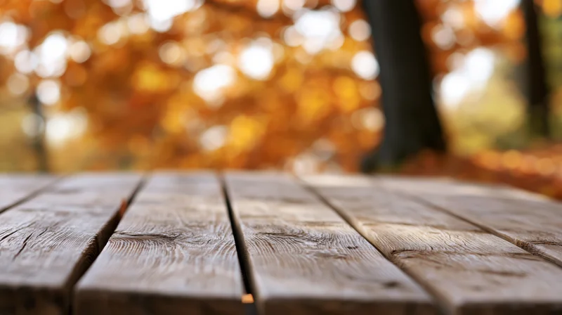 Weathered wooden table surface in a park with autumn foliage in the background