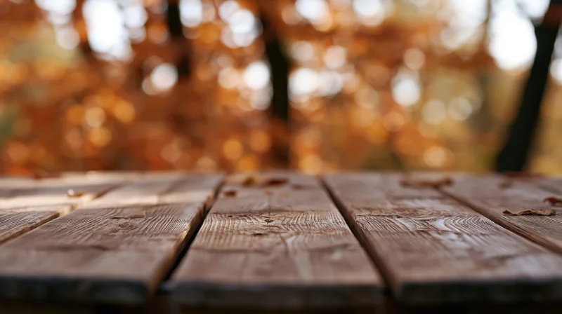 Weathered wooden plank table surface in an autumn park setting with blurred foliage background