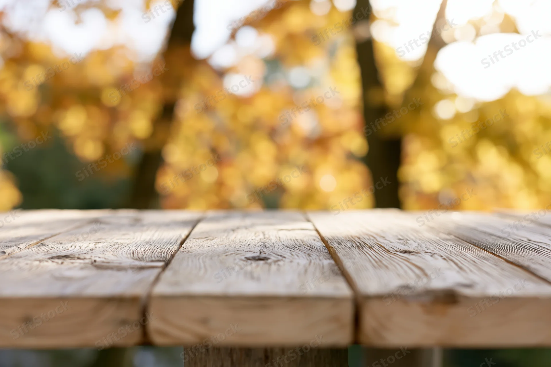 Weathered wooden table surface in autumn park setting with blurred foliage background