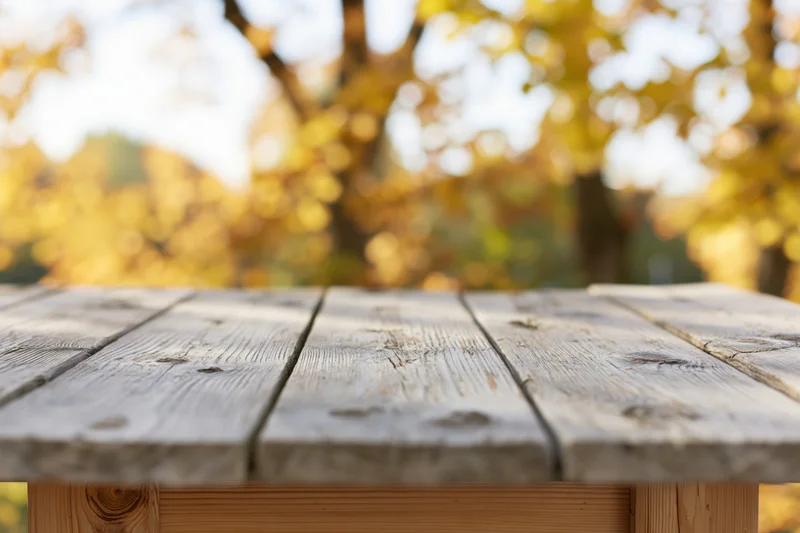 Weathered wooden plank tabletop outdoors with autumn foliage in soft focus background