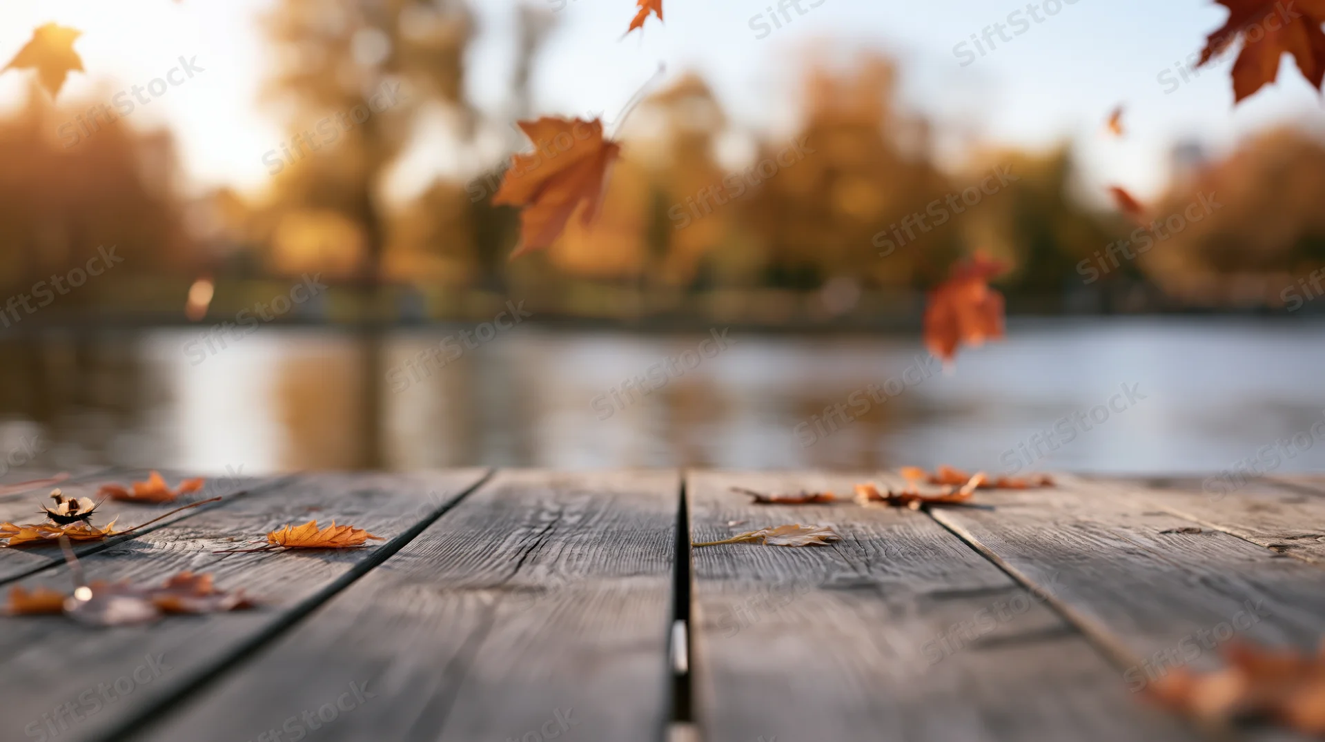 Weathered wooden table with autumn leaves scattered on surface near lake at sunset