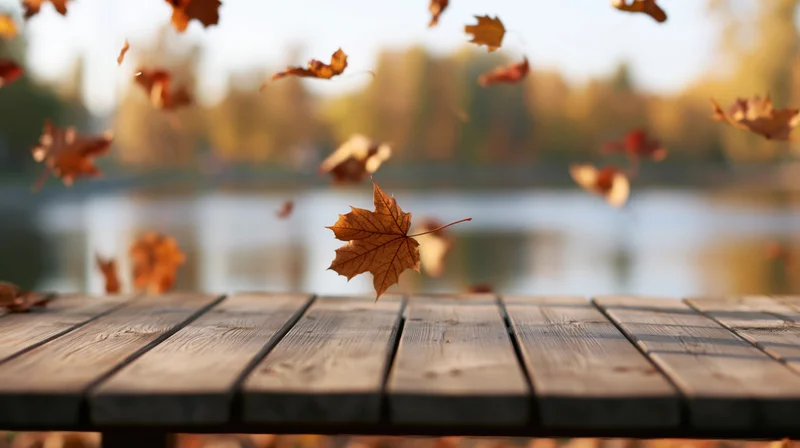 Falling maple leaves over a weathered wooden table by a lake in autumn