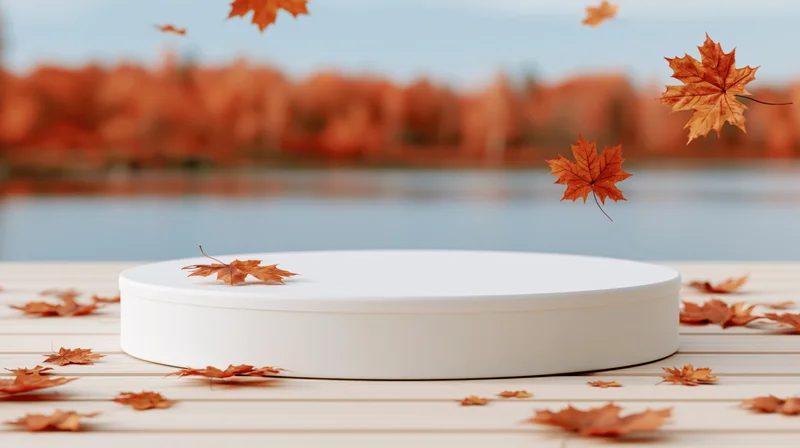 White round display platform on wooden deck with falling maple leaves near lake in autumn