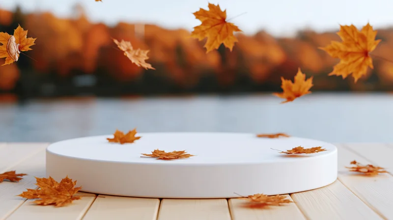 White circular display platform on wooden deck with falling maple leaves in autumn setting