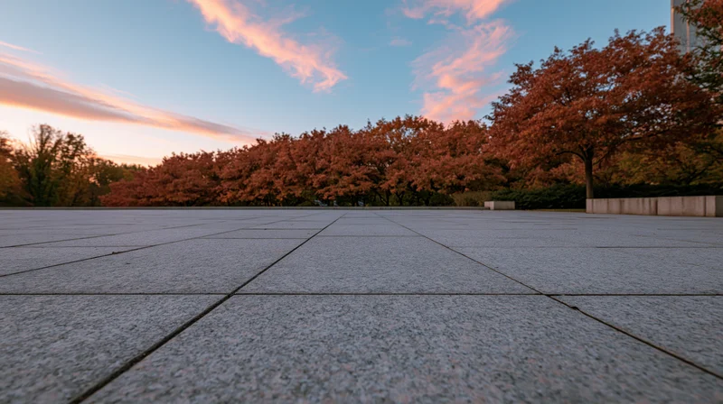 Wide granite tile plaza stretching to horizon with autumn trees and sunset sky