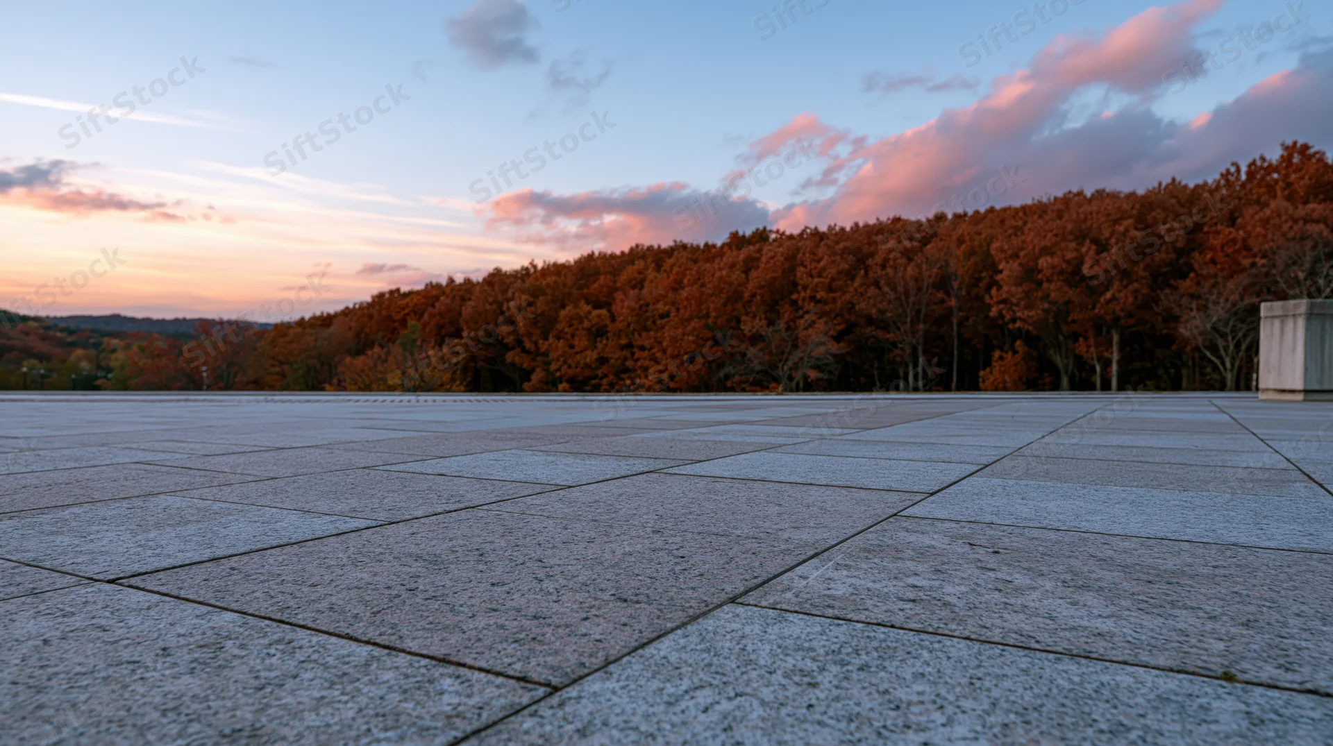 Wide granite tile plaza stretching to horizon with autumn trees and sunset sky