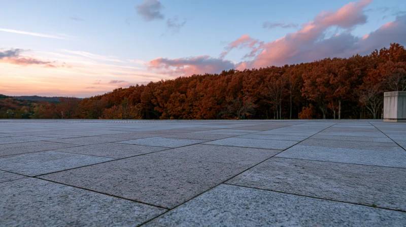 Wide granite tile plaza stretching to horizon with autumn trees and sunset sky