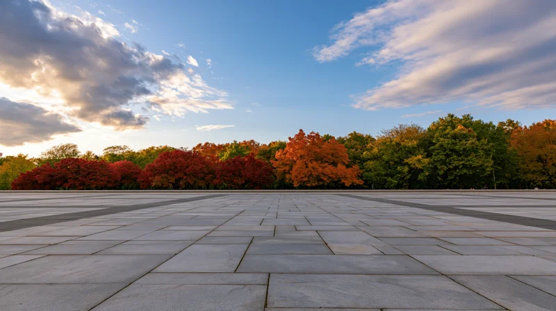 Wide granite tile plaza stretching to horizon with autumn trees under cloudy sky