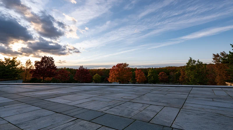 Wide granite tile plaza stretching to horizon with autumn trees and cloudy sky at sunset